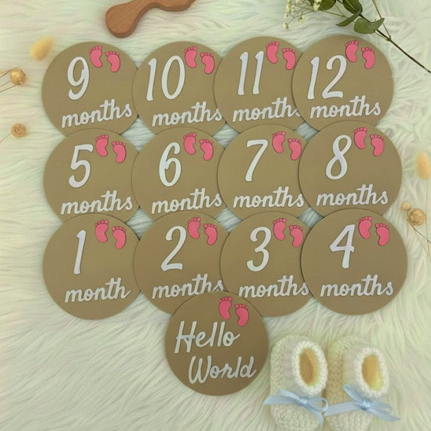 Baby milestone cards with months printed on them, placed on a soft surface with decorative elements.